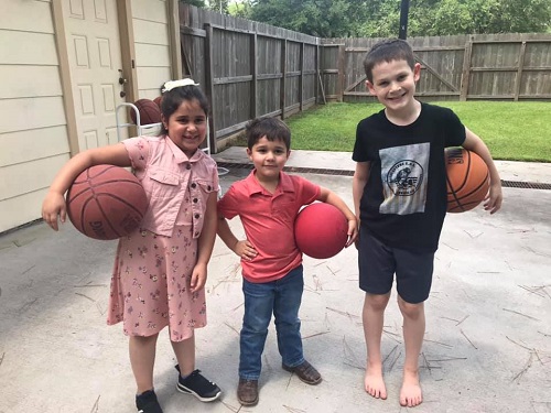 three students holding basketballs on an outside basketball court